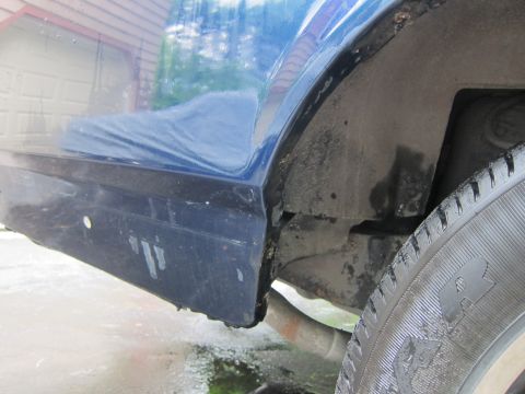 1991 Ford LTD Crown Victoria - Detail shot of the rear wheel well and lower body of a blue vehicle, showing signs of wear and tear.