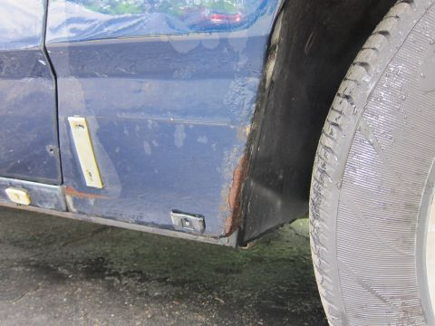 1991 Ford LTD Crown Victoria - Close-up of a blue car's side panel showing rust damage and a tire.