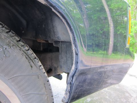 1991 Ford LTD Crown Victoria - Close-up of a black vehicle's rear quarter panel and tire, showing some damage to the panel's edge.