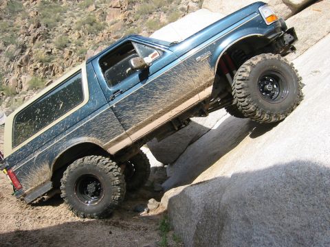 1994 Ford Bronco - This Ford Bronco is navigating a rocky, off-road trail, kicking up dirt as it climbs.
