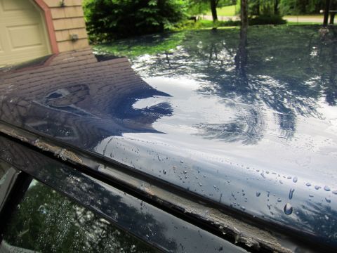 1991 Ford LTD Crown Victoria - The dark blue car roof shows significant damage and water droplets, with reflections of the surrounding environment.