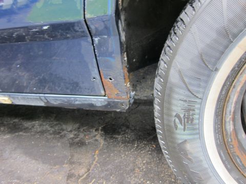 1991 Ford LTD Crown Victoria - Close-up of a rusty car door and tire, showing damage and wear on the vehicle's exterior.