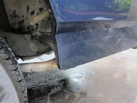 1991 Ford LTD Crown Victoria - Close-up view of a blue car's lower body panel and tire, showing signs of rust and wear.