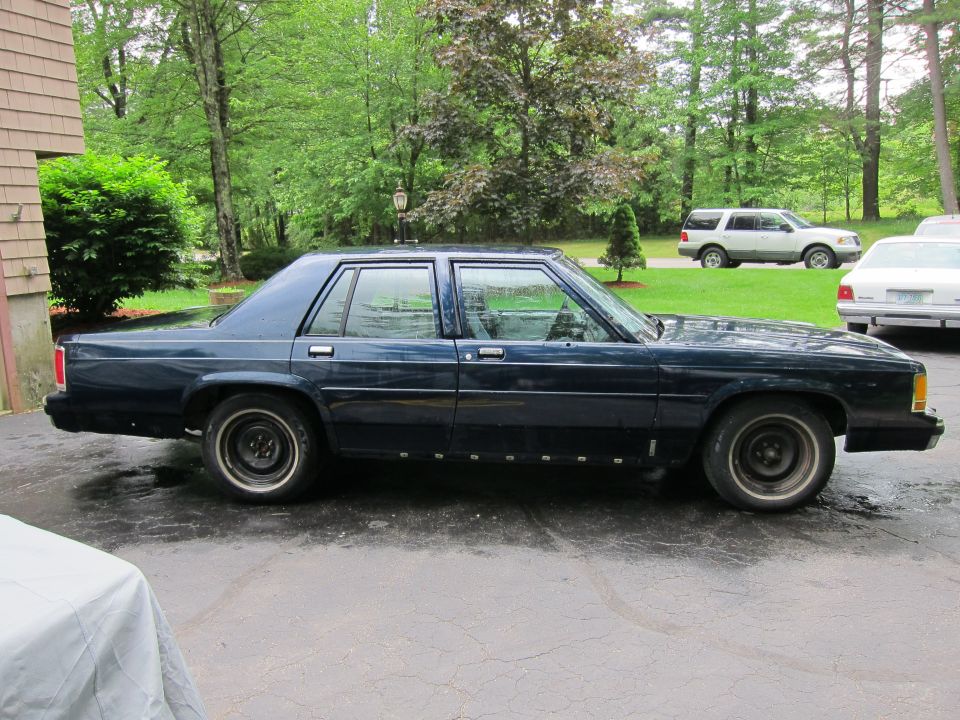 Dark blue sedan parked on asphalt, side view. Appears to be a Ford Crown Victoria from the early 1990s