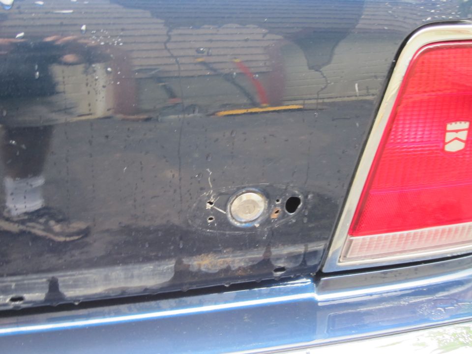 Close-up of a dark blue sedan's rear, showing a missing fuel door and part of a red taillight