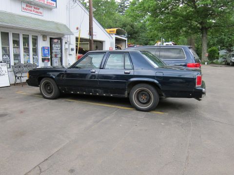 1991 Ford LTD Crown Victoria - A dark 1991 Ford Crown Victoria LTD sedan is parked outside a body shop.