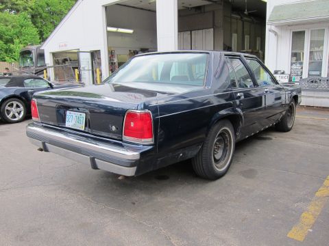 1991 Ford LTD Crown Victoria - A dark blue sedan is parked in front of a garage with another car visible to the left.