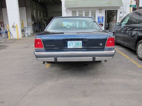 1991 Ford LTD Crown Victoria - A dark blue sedan is parked next to a dark minivan, with the sedan's rear visible.
