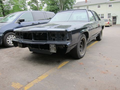 1991 Ford LTD Crown Victoria - A dark-colored sedan, possibly a 1991 Ford Crown Victoria LTD, is shown with its front end disassembled in a parking lot.