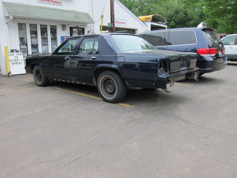 1991 Ford LTD Crown Victoria - A dark sedan is parked in a lot, showing its rear end with a missing bumper.