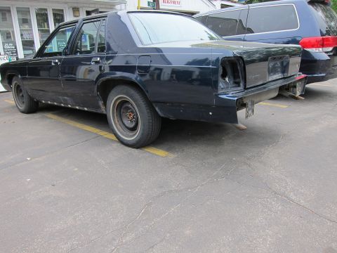 1991 Ford LTD Crown Victoria - Rear view of a dark sedan with damage to the taillight and bumper area.