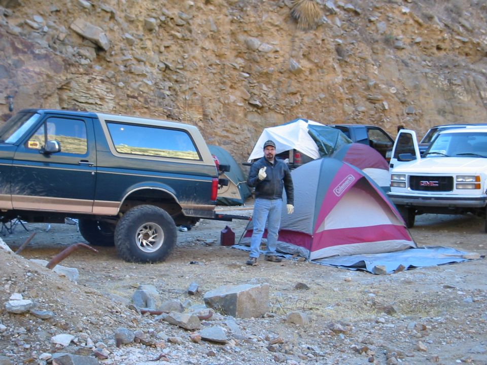 Teal two-tone lifted 1990s Ford Bronco at a rocky desert campsite, rear three-quarter