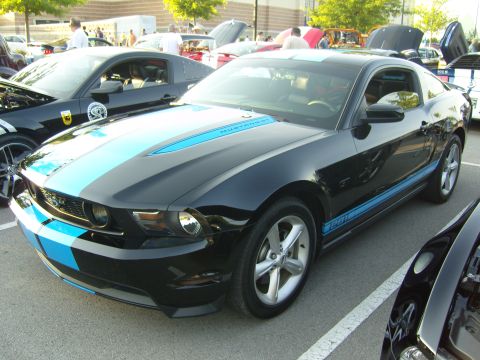 2007 Ford Mustang - A black 2007 Ford Mustang GT with distinctive blue racing stripes and side decals is parked at an outdoor event.