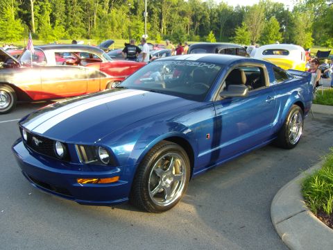 2007 Ford Mustang - A blue Ford Mustang is parked at an outdoor car show with other vehicles in the background.