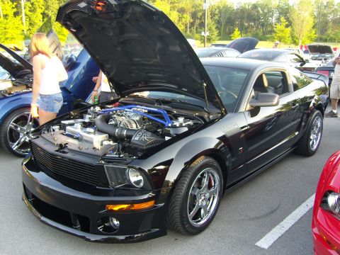 2007 Ford Mustang - A black Ford Mustang is parked with its hood open, revealing a supercharged engine and custom blue bracing.