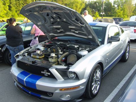 2007 Ford Mustang - A silver Ford Mustang with blue racing stripes is parked with its hood open, revealing the engine compartment.