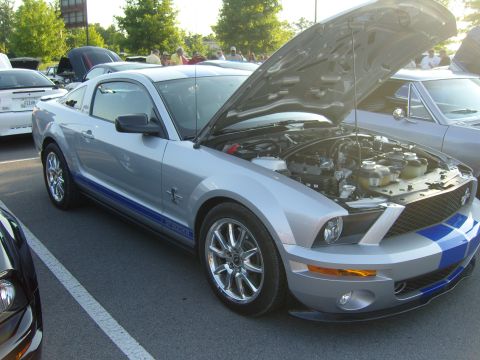 2007 Ford Mustang - A silver 2007 Ford Mustang GT500 with blue racing stripes is parked with its hood open, revealing the engine compartment.