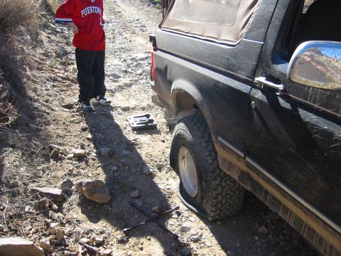 1994 Ford Bronco - Flat tire on a 1994 Ford Bronco on a rough dirt road, with a person standing nearby.