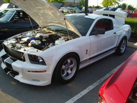 2007 Ford Mustang - A white 2007 Ford Mustang Shelby GT500 is parked with its hood open, revealing the engine and a glimpse of its red interior.