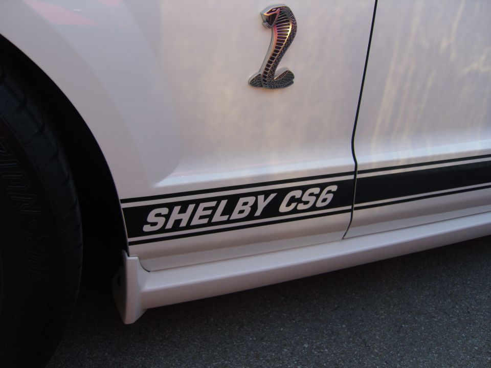 Side view of a white car with black Shelby CS6 stripe and cobra badge