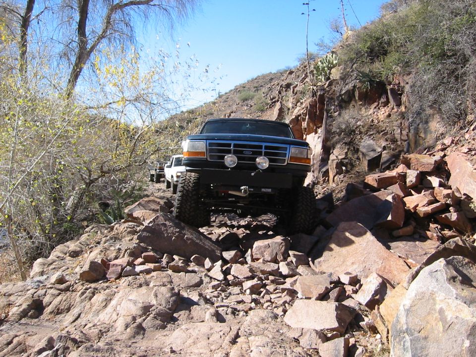 Dark Ford Bronco with winch bumper crawling a rocky desert trail, head-on view