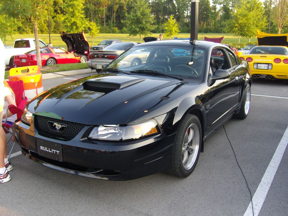 Black Ford Mustang with a hood scoop and 'Bullitt' plate, parked in a lot