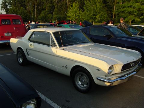 2007 Ford Mustang - A classic white Ford Mustang is parked in a lot with other vehicles during an outdoor gathering.