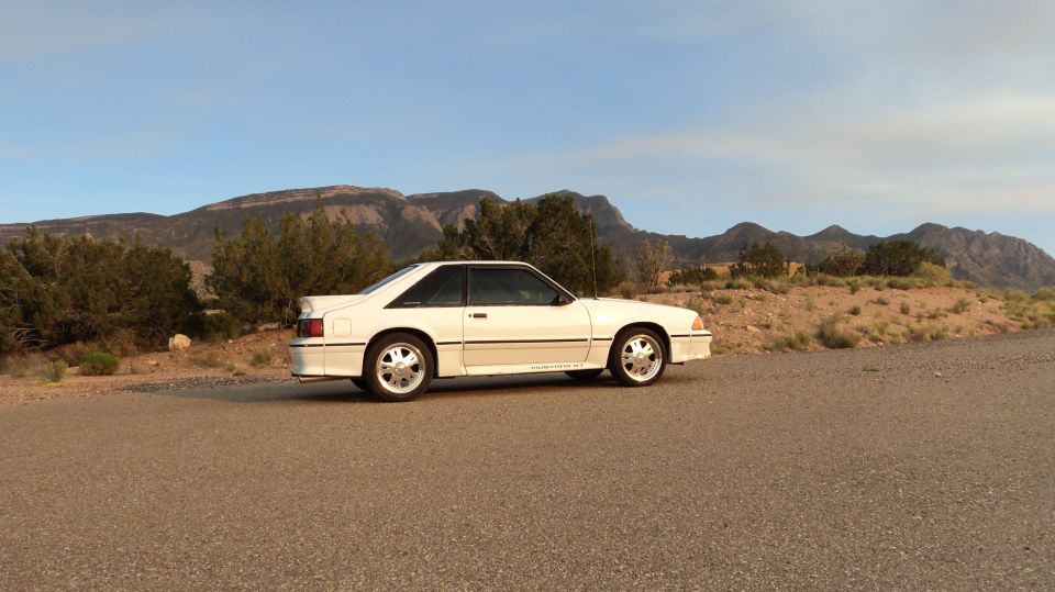 White coupe car parked on a dirt road with mountains in the background