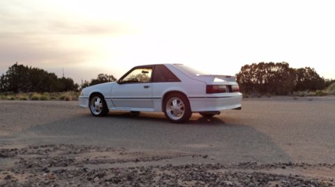 1989 Ford Mustang - Rear view of a white 1989 Ford Mustang coupe parked on a dirt road at sunset.