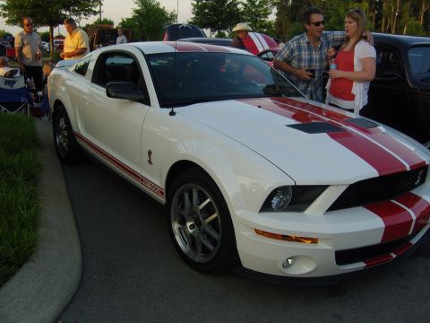 2007 Ford Mustang - A white 2007 Ford Mustang GT500 with red racing stripes is parked at an outdoor event with people around.