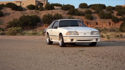 1989 Ford Mustang - White 1989 Ford Mustang parked outdoors with a desert-like landscape behind it.
