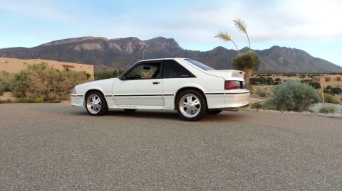 1989 Ford Mustang - A white Ford Mustang GT is parked outdoors with a desert landscape and mountains in the distance.