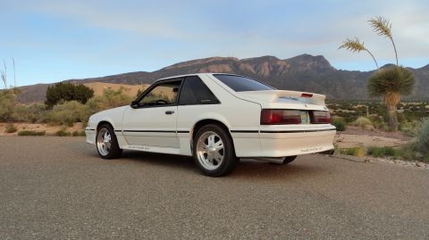 1989 Ford Mustang - A white 1987 Ford Mustang GT coupe is viewed from the rear three-quarter angle in a desert landscape.