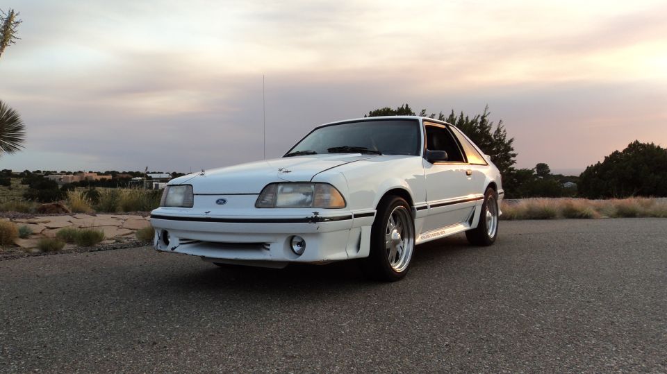 White 1989 Ford Mustang coupe with body kit parked on asphalt