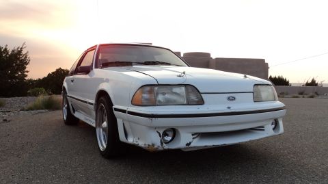 1989 Ford Mustang - A white Ford Mustang is parked outside during sunset, showing its front end and side profile.