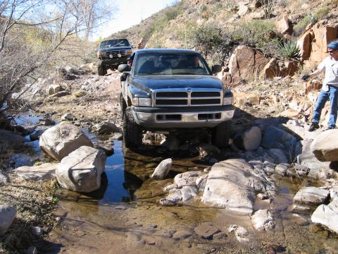 1994 Ford Bronco - Two trucks, a 1994 Ford Bronco and a Dodge Ram, off-roading on a rocky trail.