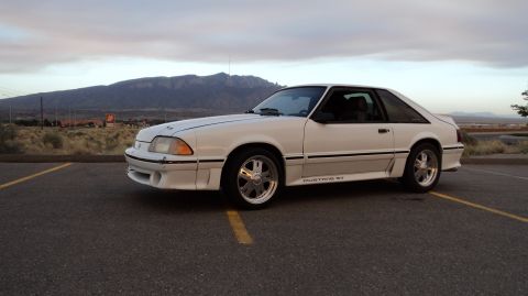 1989 Ford Mustang - A white Ford Mustang GT is parked in a lot with mountains visible in the distance.