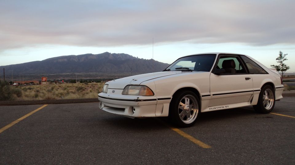 White 1989 Ford Mustang GT coupe parked in a lot with mountains in the background