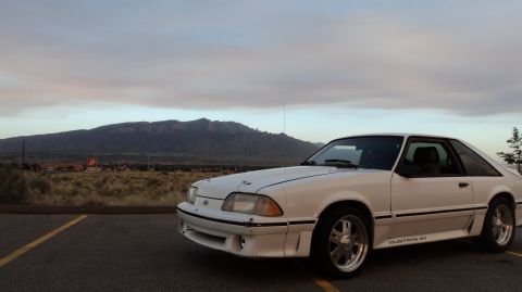 1989 Ford Mustang - 1989 Ford Mustang GT parked in a lot with a mountain range in the background under a cloudy sky.