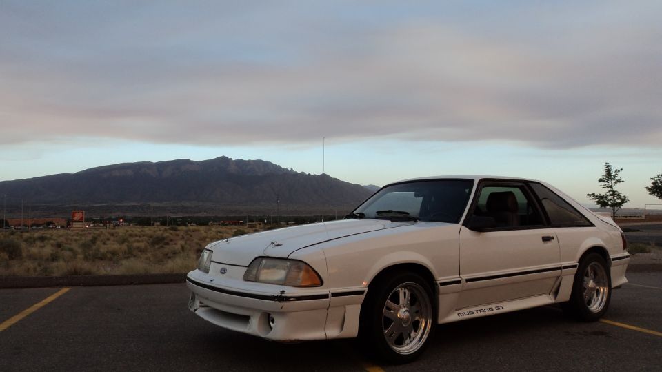 White Ford Mustang hatchback parked with mountains in background