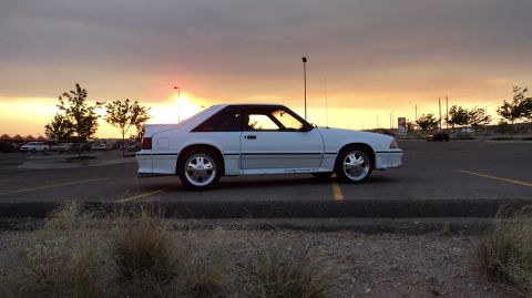 1989 Ford Mustang - A white 1989 Ford Mustang GT coupe is parked in a lot during a sunset.