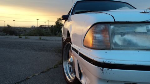 1989 Ford Mustang - A white 1989 Ford Mustang is captured in a close-up shot during sunset, highlighting its front corner.