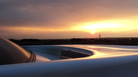 1989 Ford Mustang - A car's hood and windshield are visible in the foreground as the sun sets on the horizon.