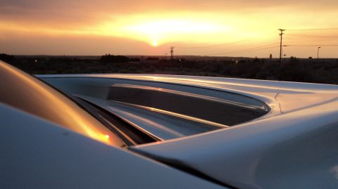1989 Ford Mustang - The sun sets behind a white car, casting a warm glow on its distinctive roof louvers.