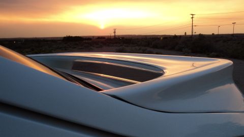 1989 Ford Mustang - Rear spoiler of a car is visible during a sunset with utility poles in the background.