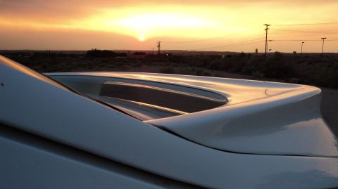 1989 Ford Mustang - The sun sets behind a car's spoiler, casting a warm glow over the landscape.