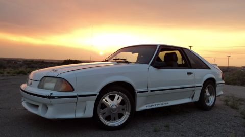 1989 Ford Mustang - A white Ford Mustang GT coupe is seen from a three-quarter front angle during a sunset.