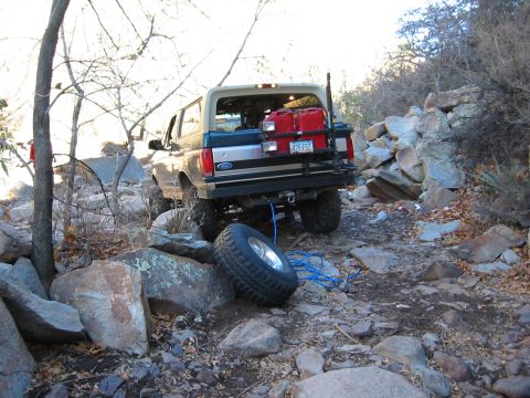 1994 Ford Bronco - A Ford Bronco navigates a challenging rocky terrain, with a spare tire dislodged and a tow rope attached.