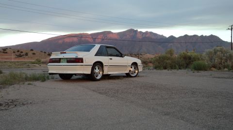 1989 Ford Mustang - A white Ford Mustang is parked outdoors with mountains in the distance.