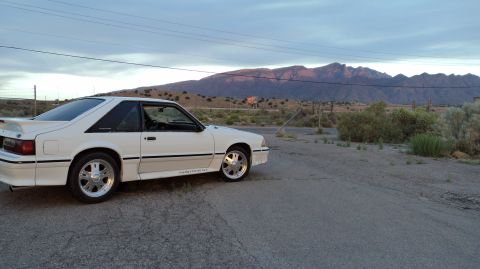 1989 Ford Mustang - A white 1989 Ford Mustang GT coupe is parked on the side of a road with mountains in the distance.